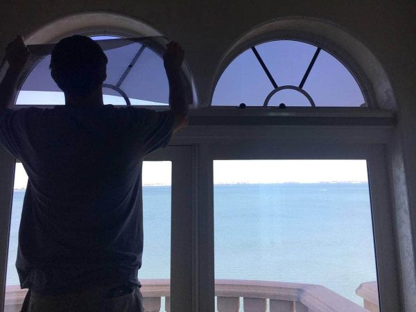 Man installing window film on half-circle windows above doors to oceanfront balcony.