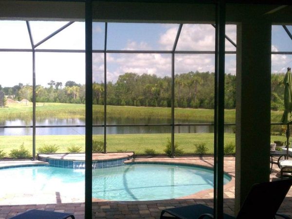 View through tinted sliding glass doors to a screened lanai, pool, and lake