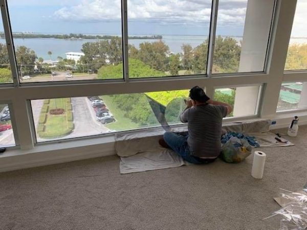NBI Suncontrol installer applying 3M window film to a floor-to-ceiling window wall with a bay view