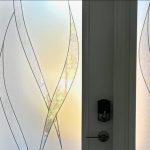 Frosted glass door with abstract wavy patterns enhanced by decorative film, featuring a metallic door handle and lock. Light gently filters through the glass panels.