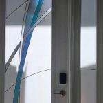 A white door with a modern design featuring frosted glass panels and blue and gray curved lines, enhanced by 3M decorative film. A digital door lock is mounted on the door.