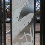 A glass door features frosted, etched designs of large tropical leaves and foliage created with 3M decorative film, allowing some light to pass through while obscuring the view outside.