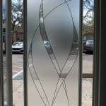 A frosted glass door features a decorative film with an abstract pattern of curved lines, partially open to reveal cars and trees in the parking lot outside.