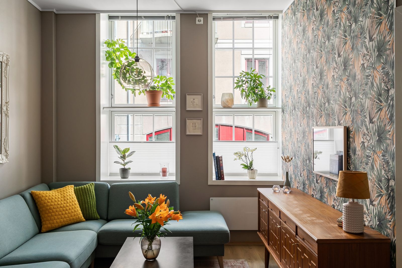Sofa, wood furniture, and plants sitting in direct sunlight near two windows