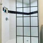 A modern shower with white subway tiles, a black horizontal tile accent, a recessed shelf, and a glass partition featuring a black grid frame enhanced by 3M decorative film.