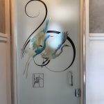 Frosted glass door with a 3M decorative film featuring two flying cranes and black calligraphic lines, silver door handle, and a signature-like mark near the bottom.