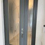 Gray front door with decorative 3M film on frosted glass panels featuring abstract curved line designs, set in a white exterior wall.