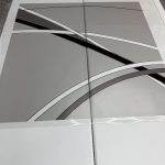 A pair of gray, white, and black vinyl decals with abstract curved line designs—perfect as decorative film—are laid out on two white folding tables.