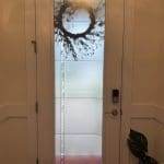 A frosted glass door with a wreath hanging on the outside, enhanced by 3M decorative film; a plant sits on the floor to the right inside the entryway.