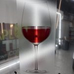 A printed image of a glass of red wine on 3M decorative film, displayed upright in an indoor setting with bright lights and blurred background elements.