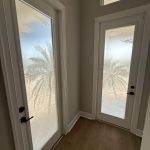 Two white framed glass doors with palm tree designs etched into frosted glass, enhanced by 3M decorative film, set in a corner with light wood flooring and beige walls.