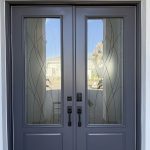 Double front doors with dark frames, vertical glass panels featuring curved line designs enhanced by decorative film, modern handles, and a keypad lock. Outdoor scenery is visible through the glass.