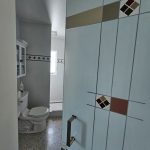 View of a bathroom through a glass door enhanced with 3M decorative film featuring geometric designs, showing a toilet, wall-mounted cabinet, and tiled floor.