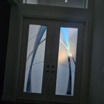 A modern double front door with frosted glass panels featuring abstract blue and gray curved lines, accented by natural light shining through premium 3M decorative film.
