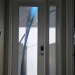 A white front door with frosted glass panels featuring blue and clear abstract designs, enhanced by natural light and a touch of 3M decorative film.