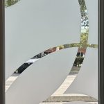 Frosted glass door with clear curved geometric patterns, enhanced by decorative film, showing a partial view of a parking lot and trees outside.