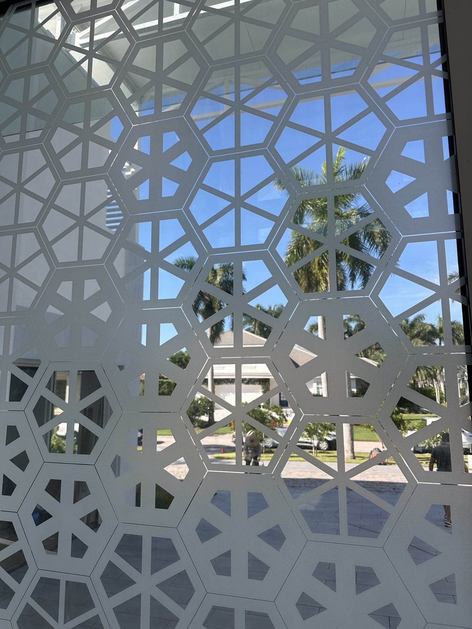 Close view of white geometric lattice decorative window film with palm trees and blue sky beyond