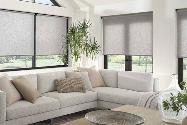 Gray roller shade window coverings on the windows of a bright living room