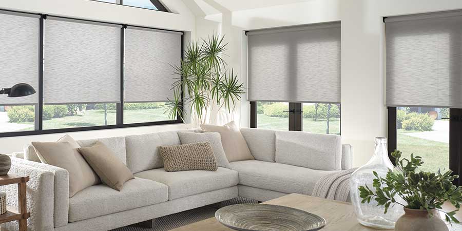 Gray roller shade window coverings on the windows of a bright living room